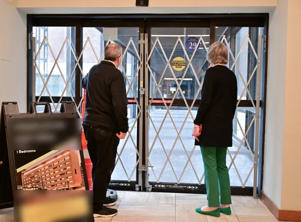 Two people look through a closed folding gate across a skyway door. By Nancy Kehmeier. The man started looking second. By Nancy Kehmeier.